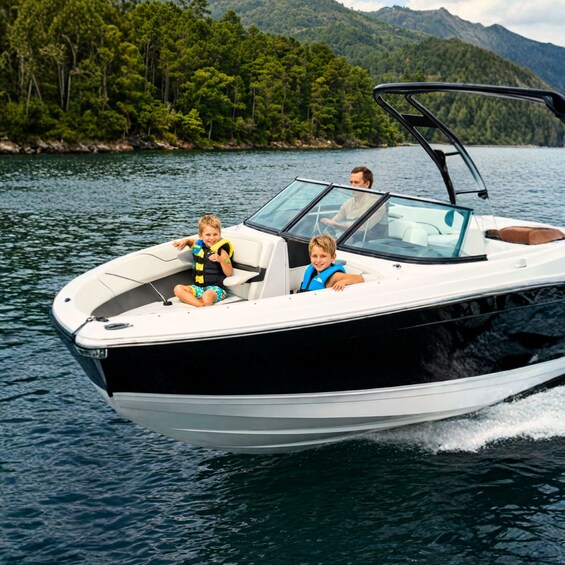 A speedboat with two passengers and a driver on a calm lake surrounded by forested hills. 5