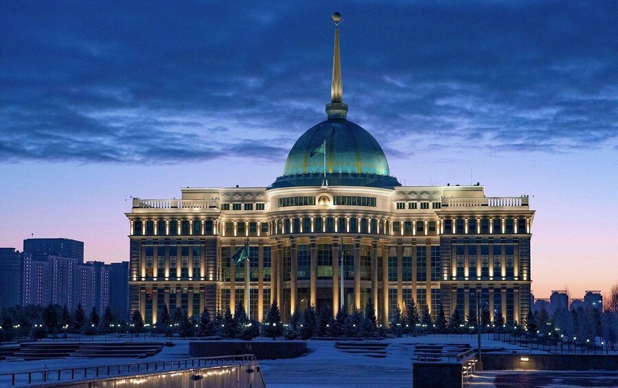 A large, ornate building with a prominent dome and a tall spire, surrounded by snow-covered trees and a frozen body of water. 3