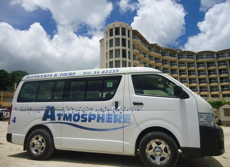 A white van with 'Atmosphere' and 'Transfers & Tours' branding parked in front of a large building. 1
