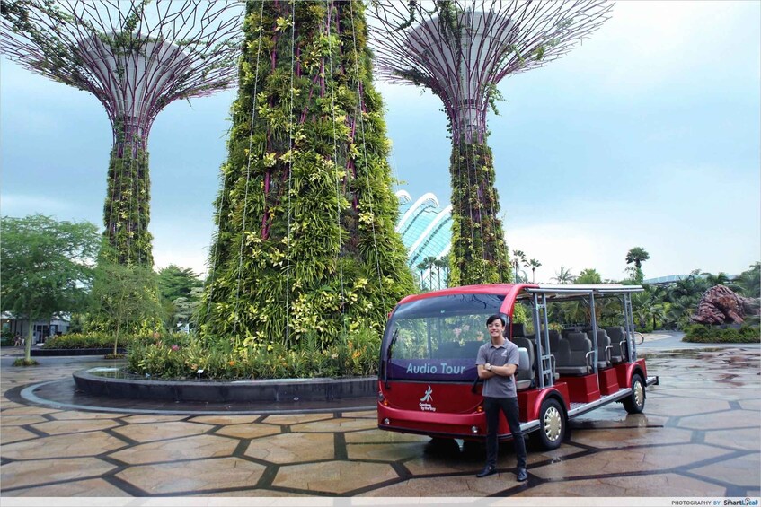 A red tour bus parked in front of a large, vertical garden structure with a blue sign. 3