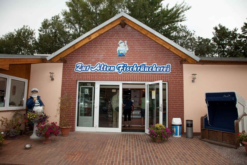 A brick building with a sign reading 'Zur Alten Fischrauchen.' There are potted plants, a statue, and a covered seating area. 1