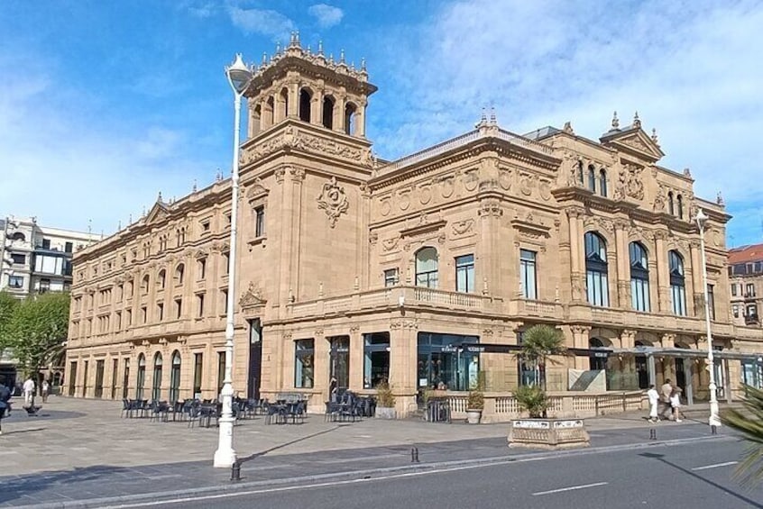 A historic building with ornate architecture, a central tower, and a plaza with seating. 5