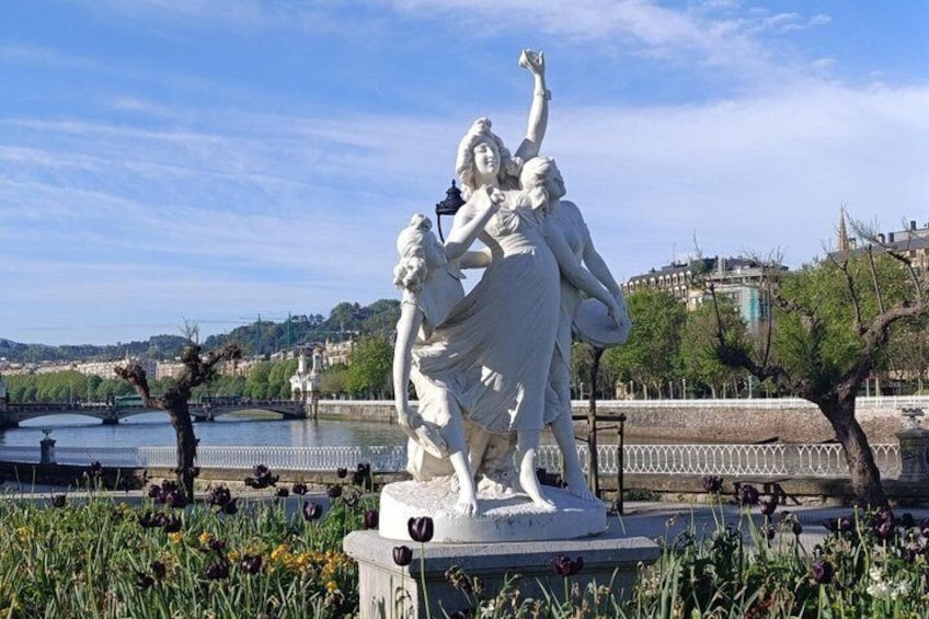 A statue of a woman with a child, surrounded by greenery and a river in the background. 3