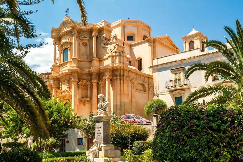 A historic building with ornate architecture, palm trees, and statues. 2