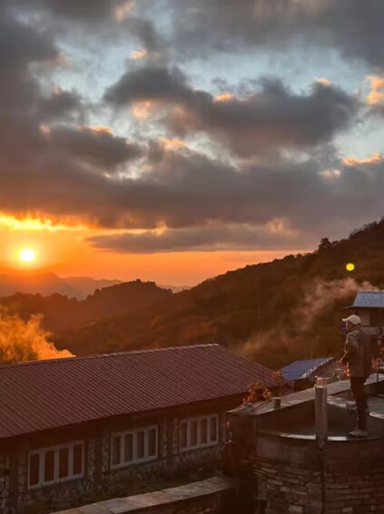 A sunset over a mountainous landscape with a person standing on a rooftop. 4