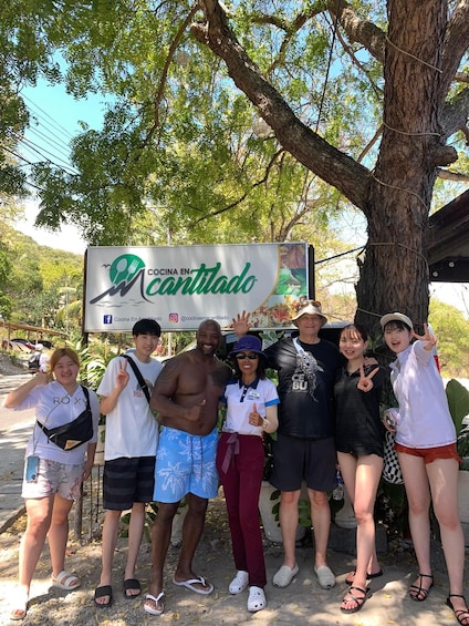 A group of people posing in front of a sign for 'Cocina En Cantilado' with a tree and a clear sky in the background. 5
