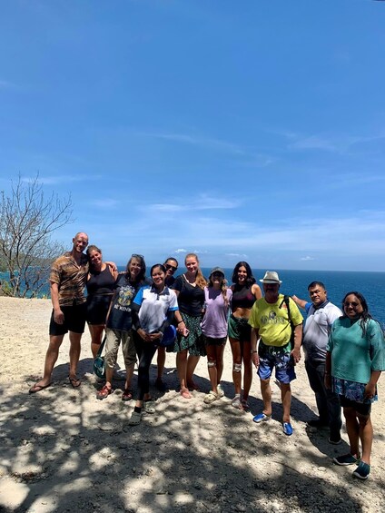 A group of people standing on a sandy beach with a clear blue sky and ocean in the background. 4