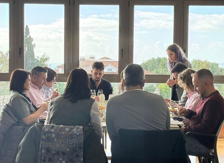 A group of people seated around a table in a room with large windows, engaged in a meal. 3