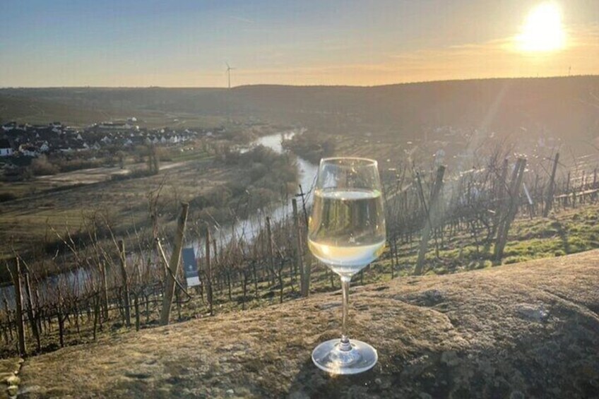 A glass of white wine on a stone ledge overlooking a vineyard with a river and houses in the distance. 5