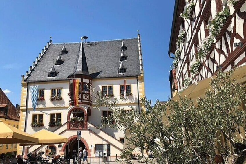 A traditional half-timbered building with a steep gabled roof, a balcony with plants, and a clear blue sky. 3