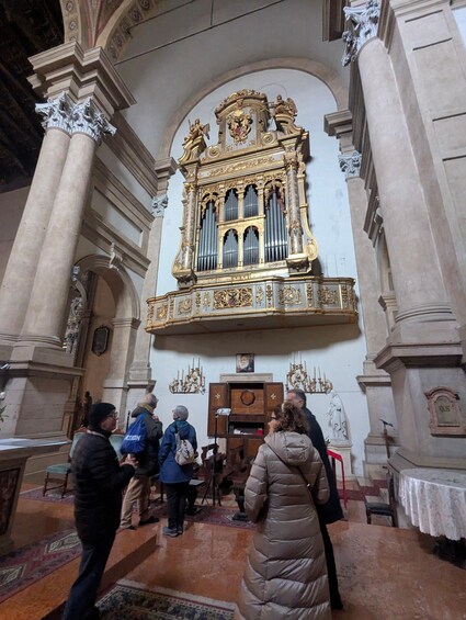 An ornate church interior with a large organ, people standing, and a statue. 5