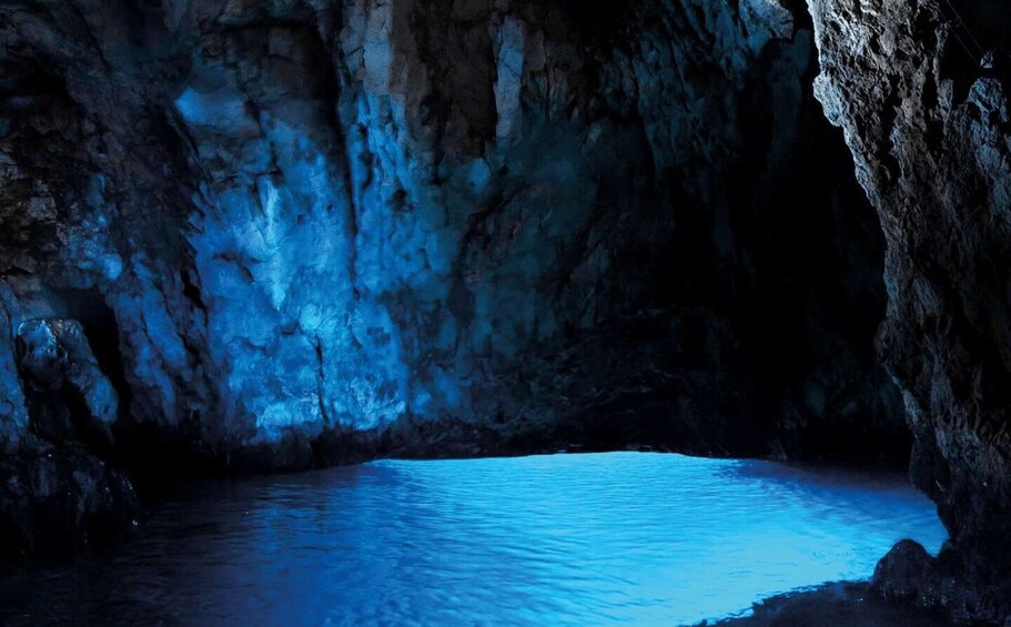 A cave with blue lighting and a pool of water. 1