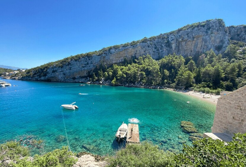 A coastal scene with clear turquoise water, boats, a wooden dock, and a rocky cliff with vegetation. 4