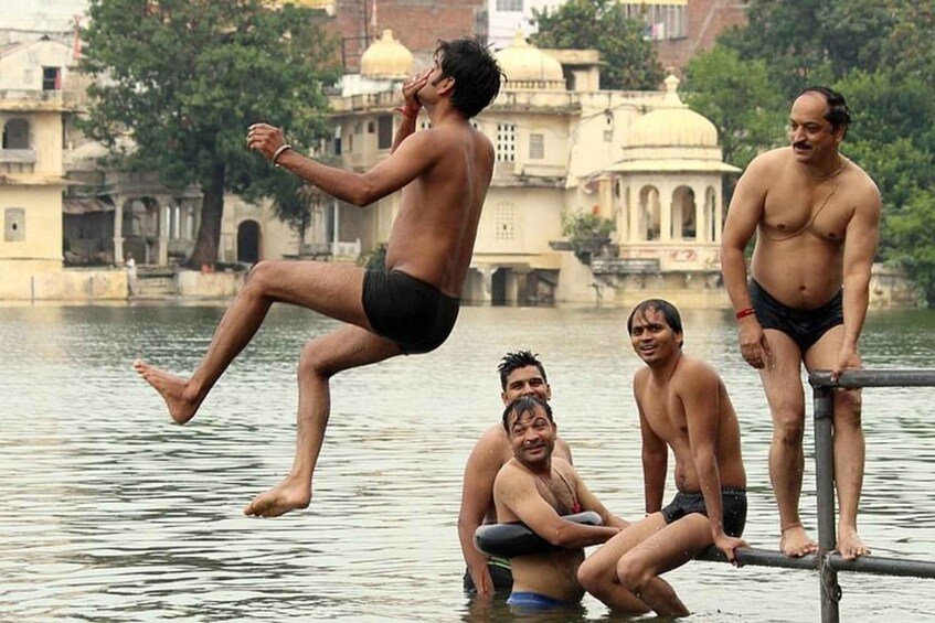 A group of men in black swim trunks near a water body with buildings in the background. 1