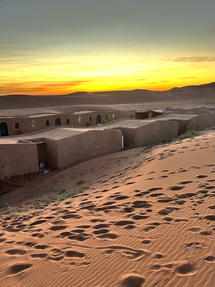 A desert landscape with sand dunes and traditional mud-brick buildings at sunset. 5