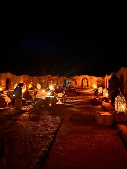 A night scene with illuminated lanterns, a rustic building, and a person sitting on a bench. 3