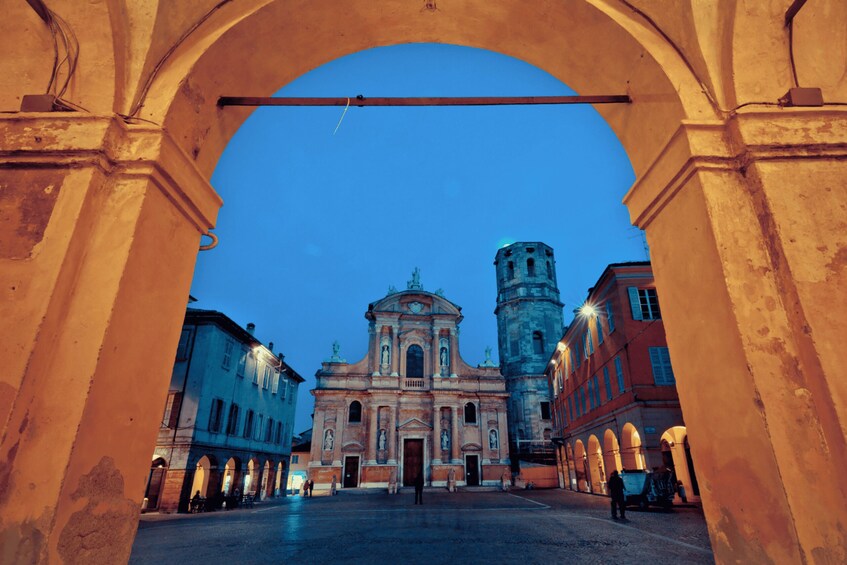 An archway framing a historic building with a bell tower, under twilight sky. 3