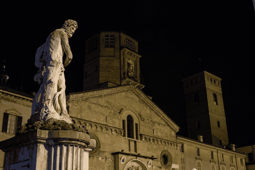 A statue on a pedestal in front of a historic building with a clock tower at night. 2