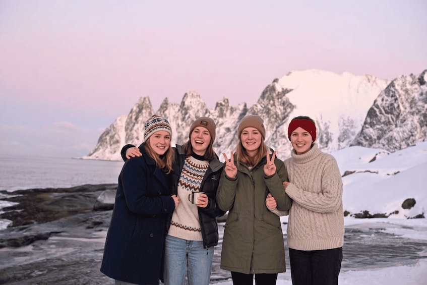 A group of people standing on a rocky shore with snow-covered mountains in the background. 2
