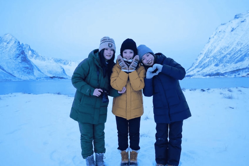 Three people standing in a snowy landscape with mountains in the background. 3