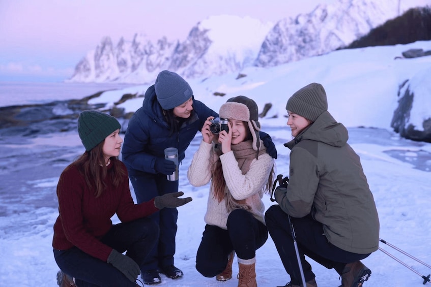 A group of people in winter clothing outdoors, with snow-covered ground and a mountainous background. 4