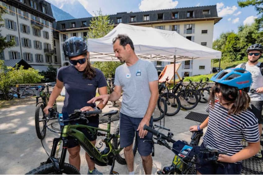 A group of people around bicycles, a tent, and buildings in a park-like setting. 4