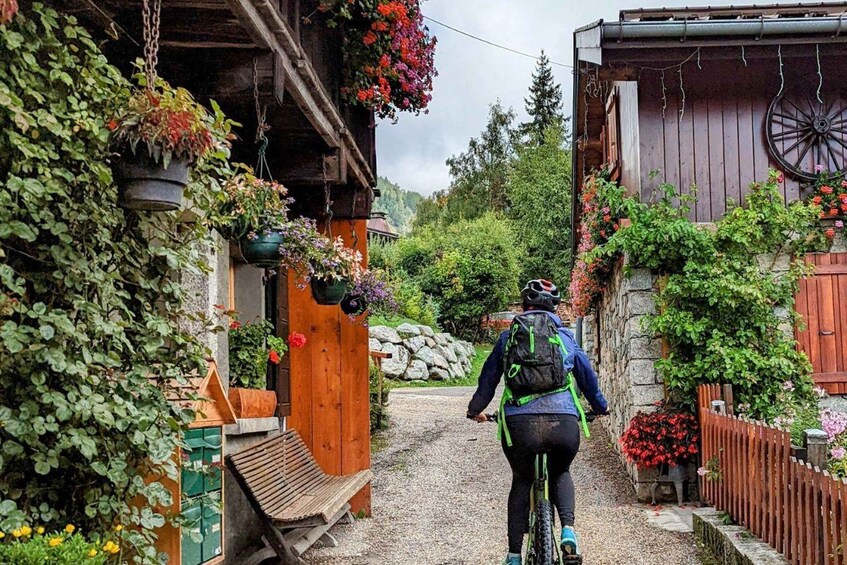 A cyclist on a gravel path in a rural area with wooden buildings and hanging flower baskets. 2