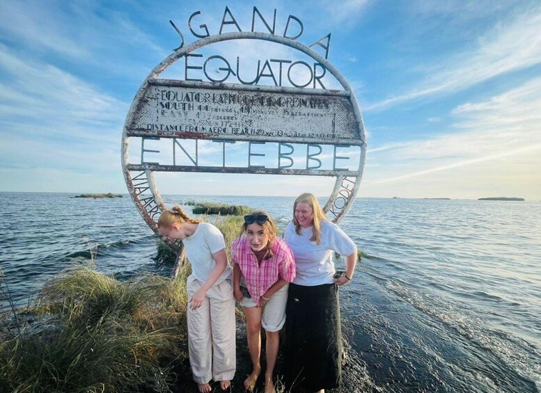 Three people standing in front of a sign with 'Equator' written on it, by the sea. 4