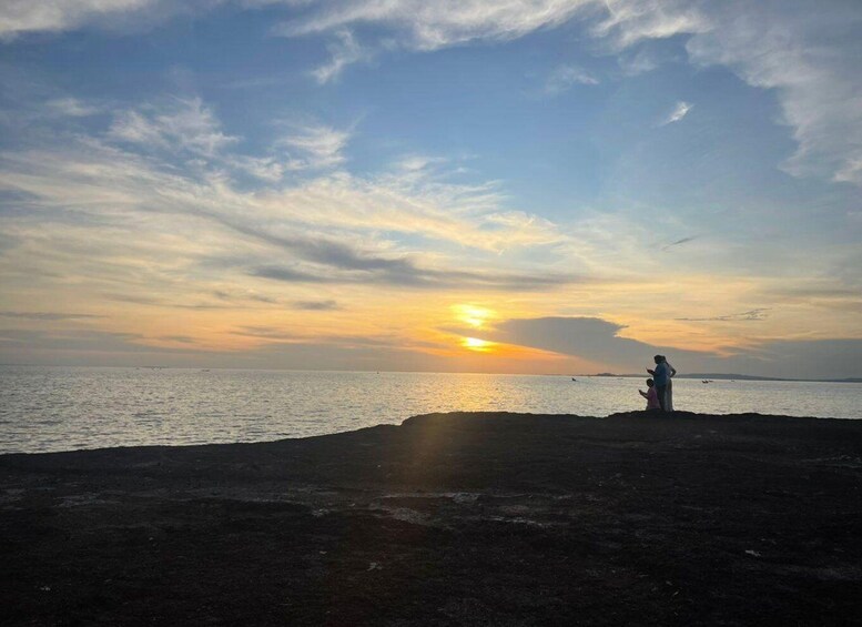 A sunset over a calm sea with a silhouette of a person and a child on a rocky shore. 5