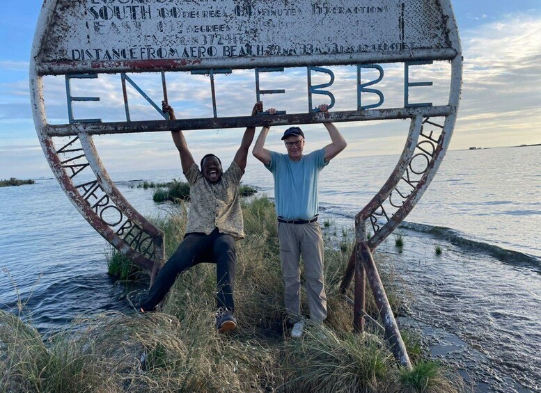 Two people posing with a weathered sign reading 'ENFERBE VIA AERO BEACH.' 3