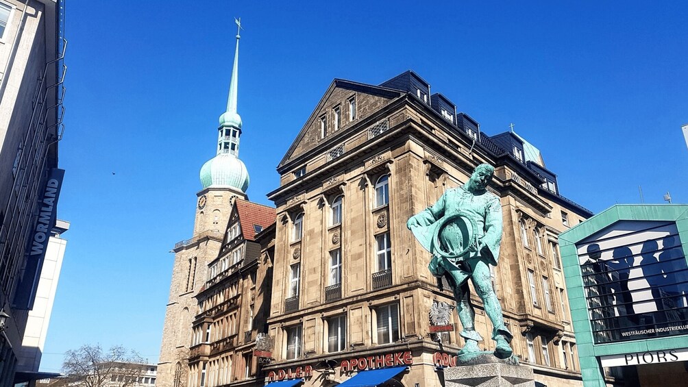 A historic building with a clock tower and a statue of a man holding a hat. 3