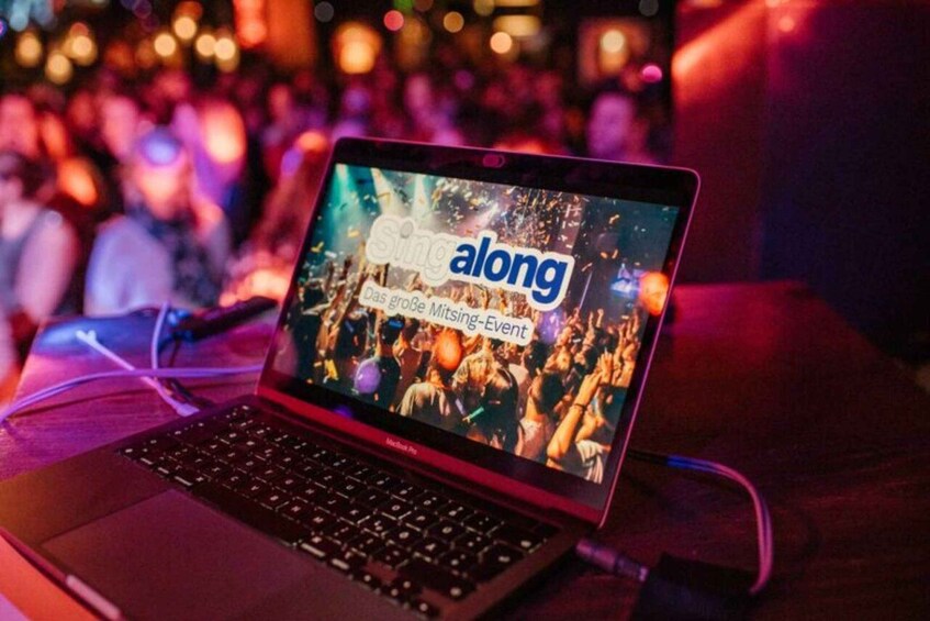 A laptop displaying a screen with the text 'along' and 'Das große Miting-Event' against a background of a crowd at a concert. 2