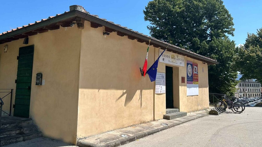 A small building with a green door, a sign reading 'Museo della Zecca,' and a bicycle parked in front. 3