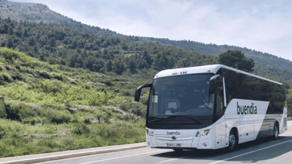 A white bus with 'buendia' branding on a road with a hilly landscape in the background. 4