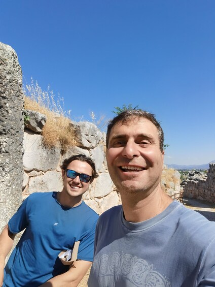 Two people standing in front of ancient ruins with clear blue skies. 4