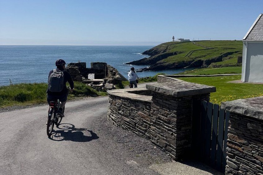 A coastal road with a cyclist, a stone wall, and a lighthouse in the distance. 5