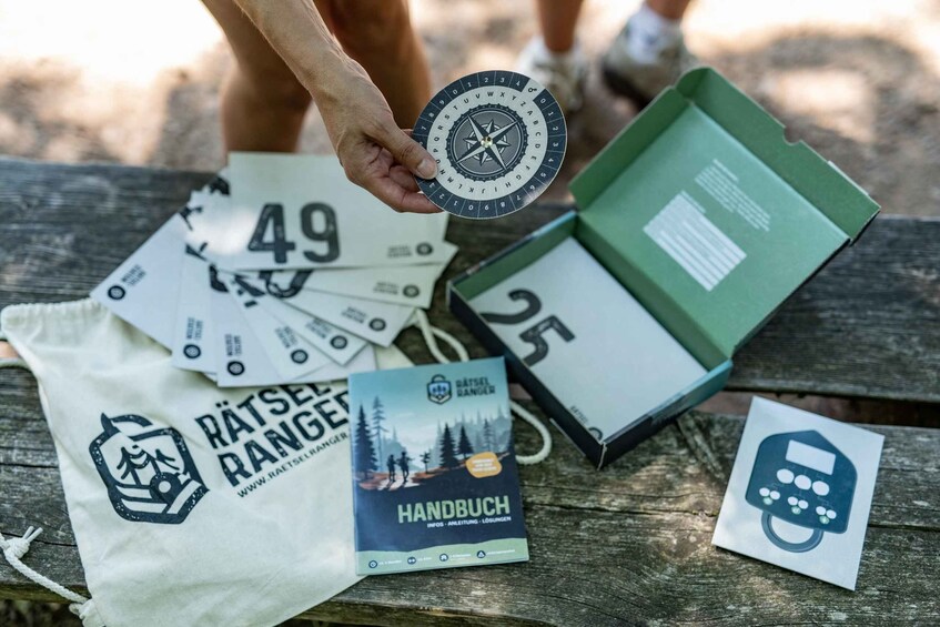 A person holding a compass, a map, and a booklet on a wooden surface. 1