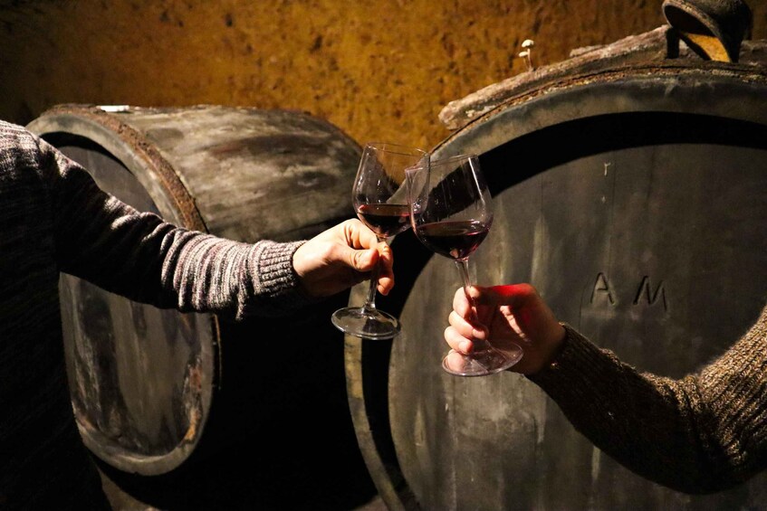 Two people holding wine glasses in front of a wooden barrel. 3