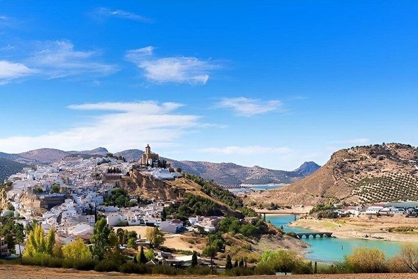 A coastal town with white buildings, a church on a hill, and a bridge over a turquoise bay. 2