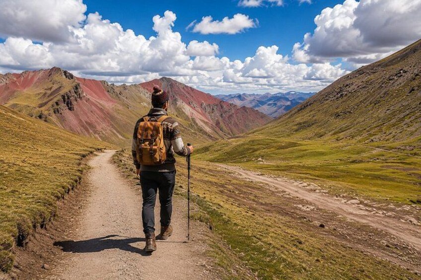A hiker on a dirt path with a backpack, surrounded by mountains and a clear sky. 5