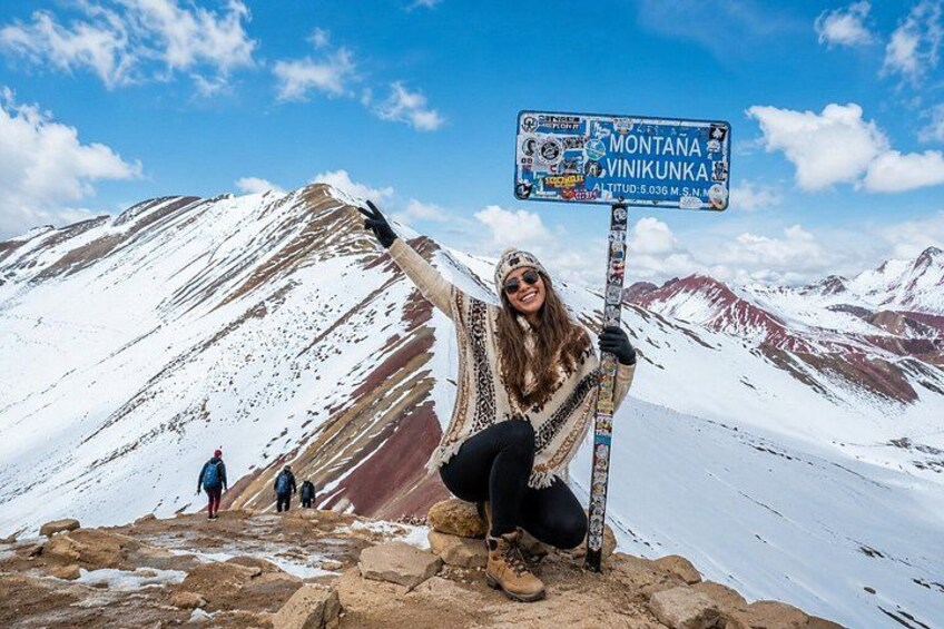 A person standing on a snow-covered mountain with a signpost, wearing a patterned jacket and gloves. 2