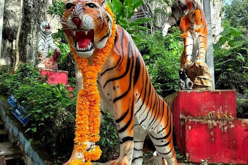 A large tiger statue adorned with orange flowers, set against a backdrop of greenery and a red wall. 4