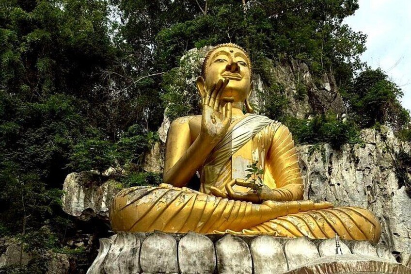 A large golden Buddha statue seated in a meditative pose, surrounded by rocky terrain and dense foliage. 1