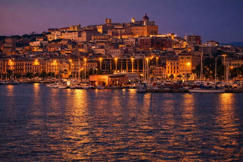 A coastal cityscape at dusk with illuminated buildings and a marina. 2