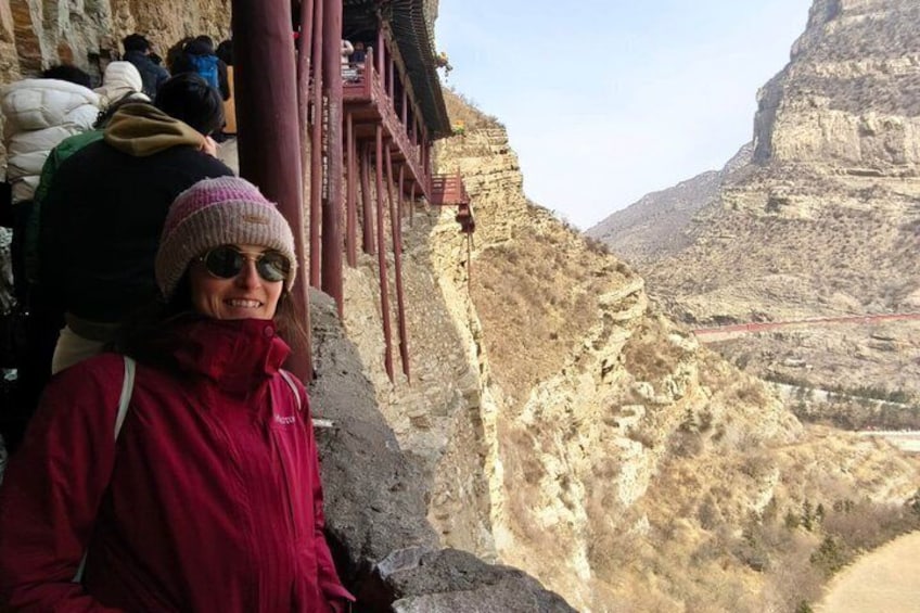 A person in a red jacket standing on a rocky ledge with a canyon in the background. 4