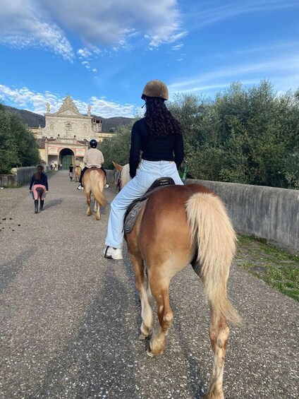 A group of people riding horses along a paved path with a historic building in the background. 2