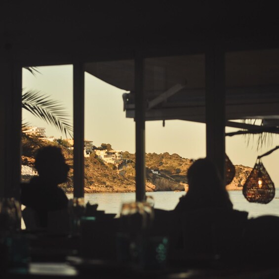 A coastal view from inside a building with large windows, overlooking a rocky shoreline with buildings on a hill. 5