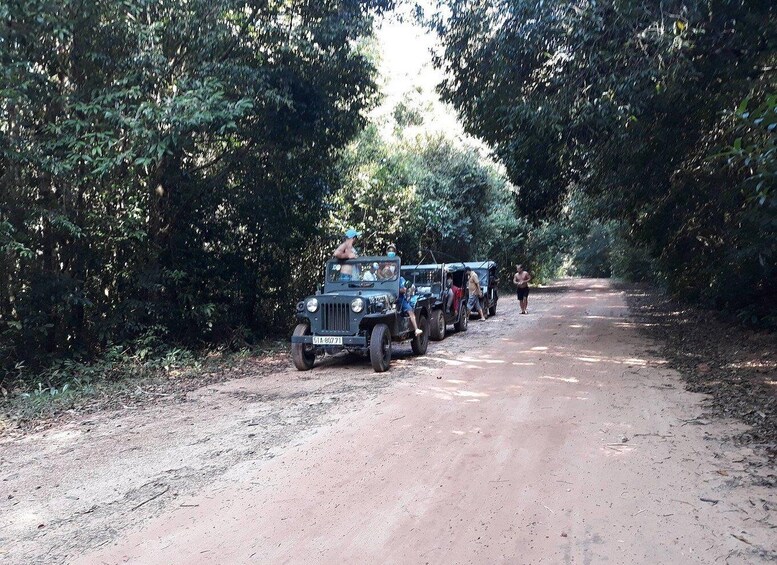 A dirt road flanked by dense foliage, with a line of off-road vehicles parked along the side. 3