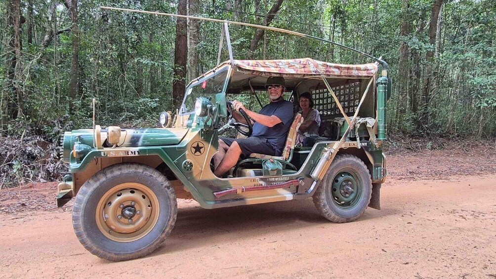 A green military jeep with a canvas roof driving on a dirt road through a forest. 4