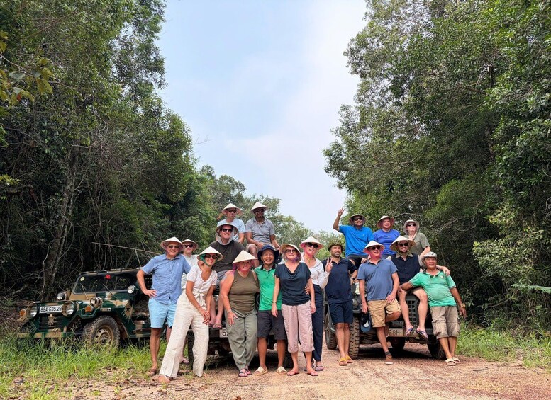 A group of people in a forested area with a green vehicle parked on a dirt path. 2